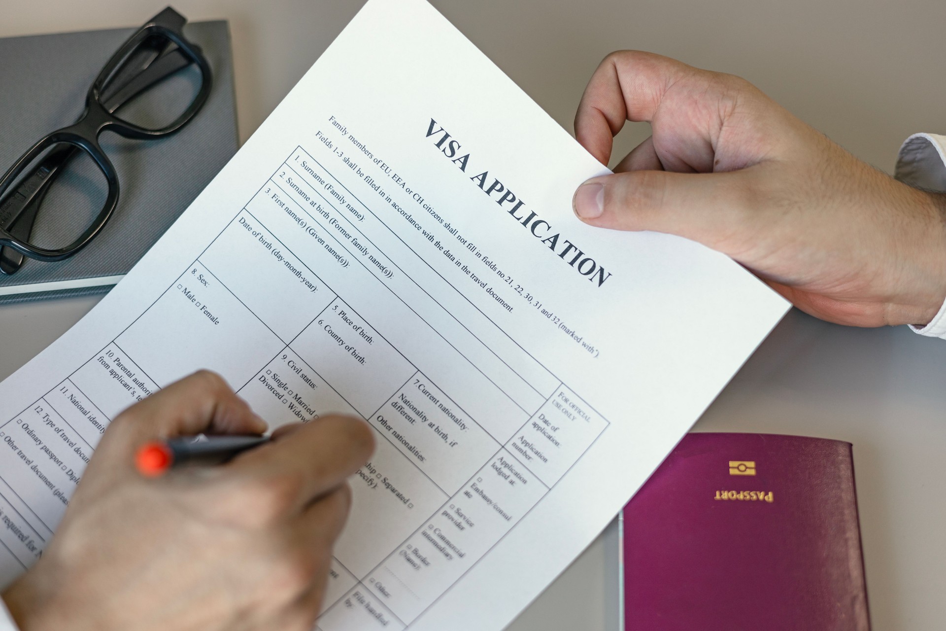 Man filling form for Visa application. Application form, hand holding pen and passport on desk.